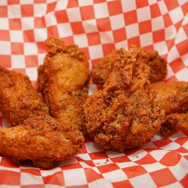 Crispy, golden-brown Wing It chicken wings, seasoned with pepper, served in a red and white checkered basket.