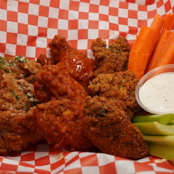 A basket of Wing It's crispy and saucy chicken wings with carrots, celery, and ranch dressing.
