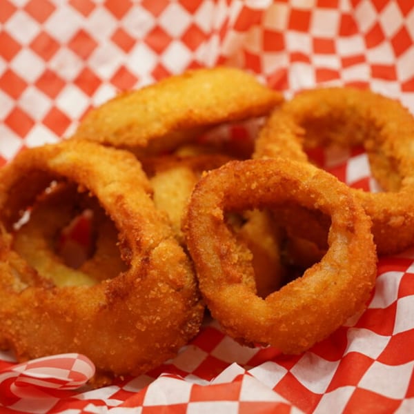Golden-brown, crispy onion rings served in a red and white checkered paper basket.