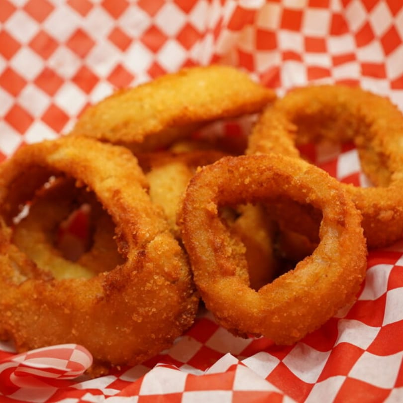 Golden-brown, crispy onion rings served in a red and white checkered paper basket.