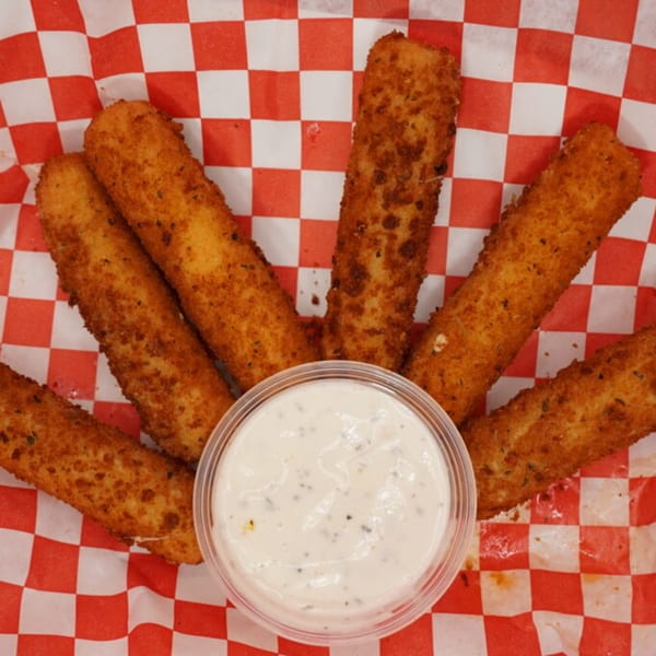 Golden-brown mozzarella sticks with a side of ranch dressing on red and white checkered paper.