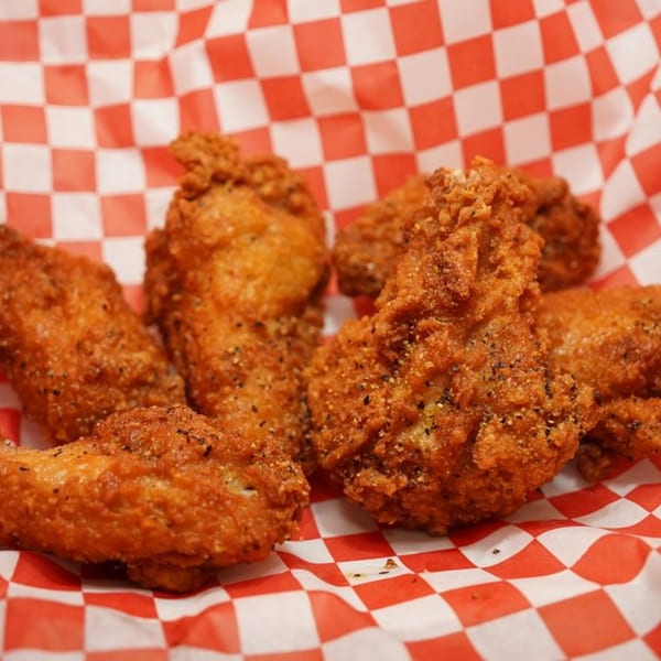 Crispy, golden-brown Wing It chicken wings, seasoned with pepper, served in a red and white checkered basket.